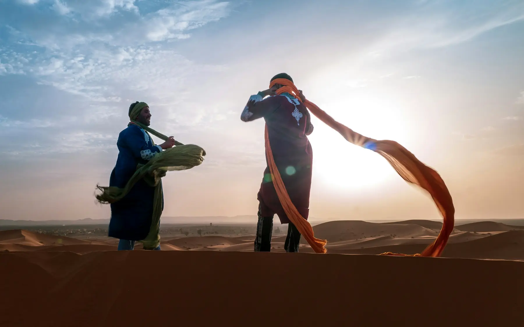 A local guide helping a traveller with a scarf in the Moroccan desert